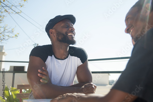 Close-up of Afro American gay men looking at each other. Two smiling bearded men sitting at table talking and spending good time together. Same sex love and gay couple relations concept