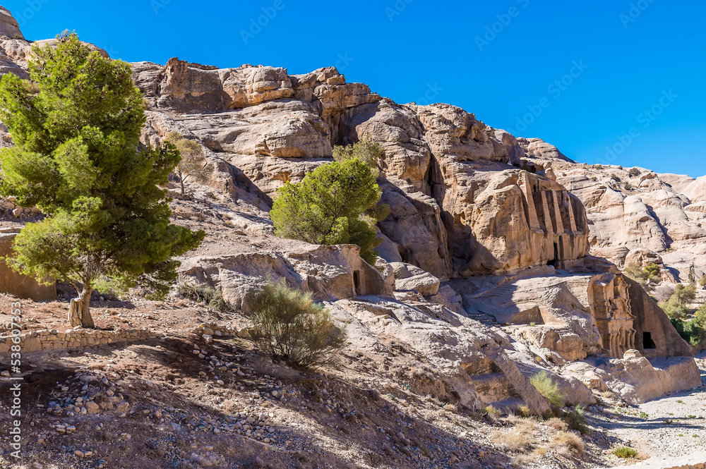 A view along the hillside past old dwellings beside the path leading to the ancient city of Petra, Jordan in summertime