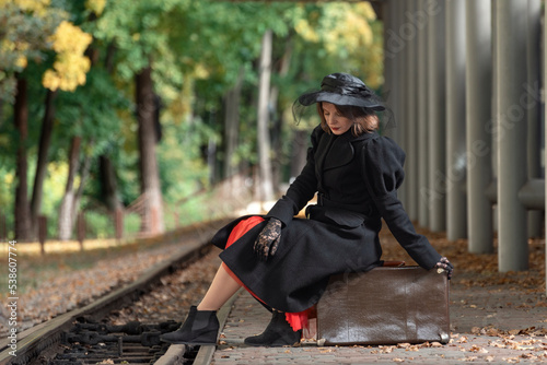 Pensive middle-aged woman with retro suitcase at train station waiting for train. Style 30-40s. Vintage clothes, autumn © somemeans