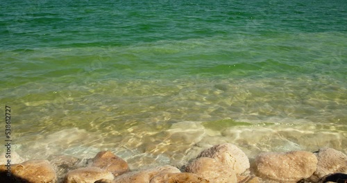 Shore of the Dead Sea. White stones covered with salt and minerals. Water is green.