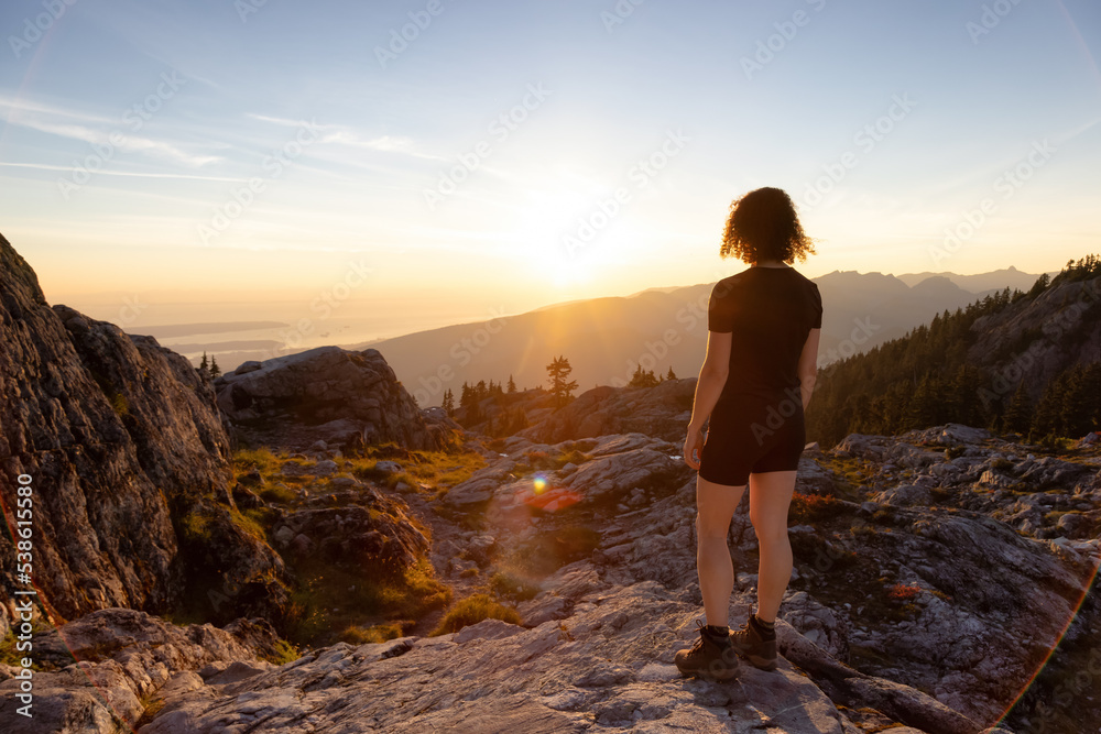 Fototapeta premium Adventurous Woman Hiker on top of Canadian Mountain Landscape. Sunny Sunset Sky. Top of Mt Seymour near Vancouver, British Columbia, Canada. Adventure Travel Concept