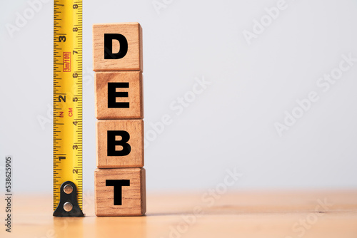 Debt wording stacking on wooden block cube with yellow tape measurement for debt analysis concept.