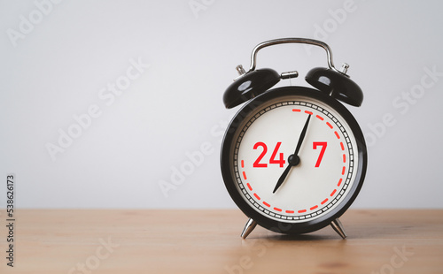 Nonstop Worldwide service available support concept , Number 24 hours and 7 days full-time contact to black alarm clock on wooden table. photo