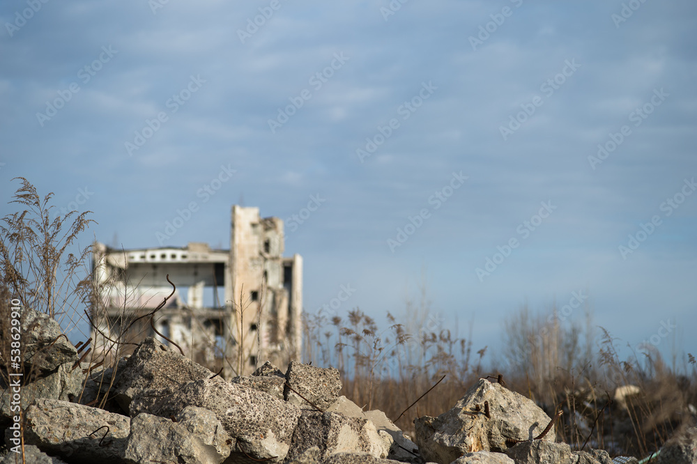 A destroyed building against a blue sky with gray clouds with a pile of concrete rubble in the foreground. Background