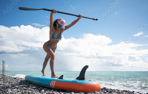Photography a sporty girl in a swimsuit with a paddle poses sexually with a sup board in sum