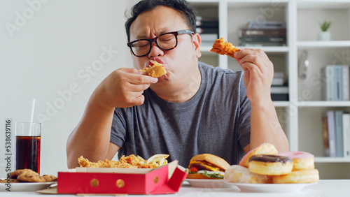 Asian fat man enjoy to eat unhealthy junk food, hamburger, pizza, fried chicken