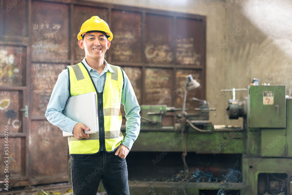 Manual workers discussing while using laptop at factory. Chief Engineer in the Hard Hat Walks Through Light Modern Factory While Holding Laptop. Smiling and happy employee. Manual workers discussing while using laptop at factory. Chief Engineer in the Hard Hat Walks Through Light Modern Factory While Holding Laptop. Smiling and happy employee.