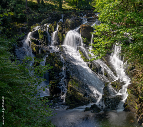 the Swallow Falls waterfall in Anglesey in northern Wales surrounded by lush green summer vegetation