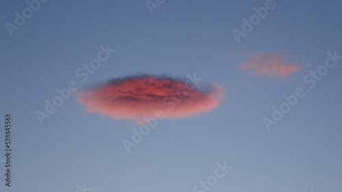 A small pink cloud in the setting sun on a blue sky.