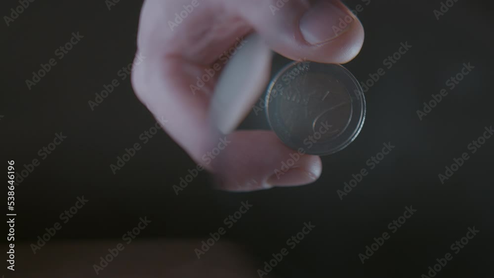 Man holding a magnifying glass and looking at a euro coin through it, selective focus, dark background