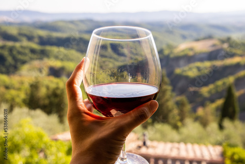 Woman holding a glass of red wine with beautiful landscape of Italy in a background on a sunny day. View from the window. photo