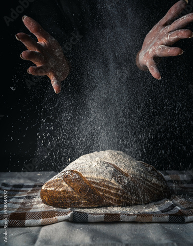 Female hands with splash of flour over a loaf of bread isolated on dark background