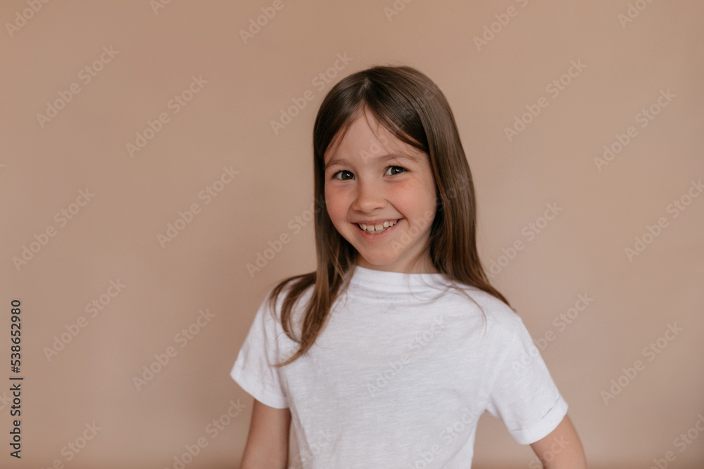 Studio shot of little european stylish girl with freckles and wonderful smile wearing white t-shirt smiling over isolated beige background Studio shot of little european stylish girl with freckles and wonderful smile wearing white t-shirt smiling over isolated beige background