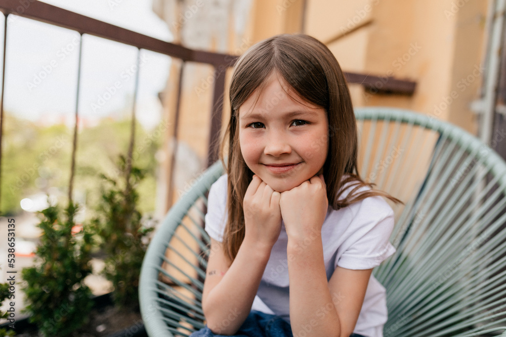 happy adorable little girl with lovely smile wearing white t-shirt sitting on the balcony in warm sunny summer day happy adorable little girl with lovely smile wearing white t-shirt sitting on the balcony in warm sunny summer day