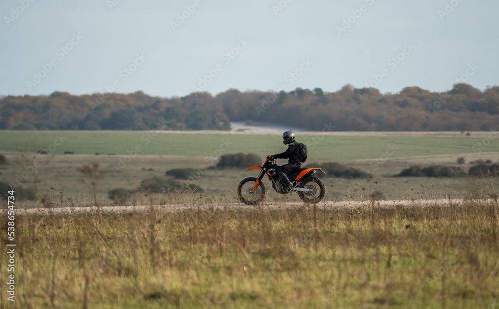 motorcyclist riding an off-road motorbike along a stone track, crossing open countryside in sunshine