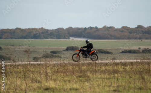 motorcyclist riding an off-road motorbike along a stone track, crossing open countryside in sunshine