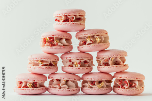 Pink strawberry macaroons decorated with golden petals and freeze-dried red berries stacked together in the shape of pyramid. White background. Close up shot