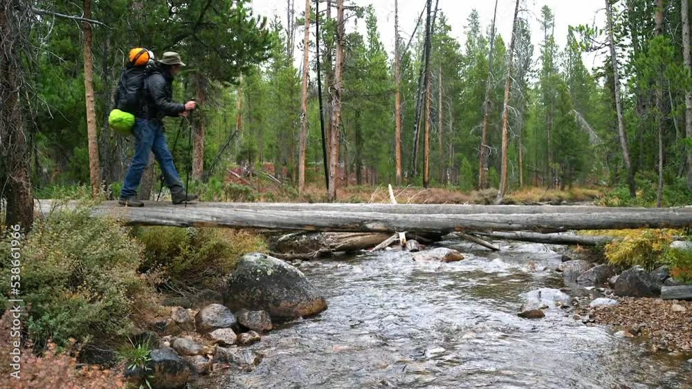 Backpacker with poles makes his way across a creek Backpacker with poles makes his way across a creek