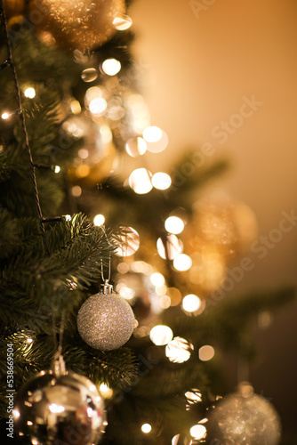 Close up view of beautiful fir branches with shiny golden bauble or ball, xmas ornaments and lights, Christmas holidays background. copy space. Decoration on christmas tree. Festive new 2023 year