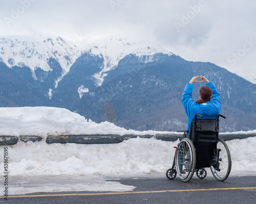 A woman in a wheelchair holds her hands in the shape of a heart in the mountains in winter.