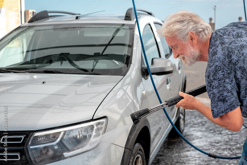 Smiling caucasian senior man washing his car in a self-service car wash station using high pressure water. Car wash self-service. Smiling caucasian senior man washing his car in a self-service car wash station using high pressure water. Car wash self-service.