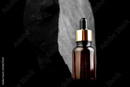Brown bottle with dropper with a beauty serum granite stone on black background. Glass packaging for cosmetic product, essential aroma oil. Skin care, hydration and nutrition with collagen.
