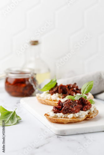 Toast with dried tomatoes in oil, cottage cheese, ricotta cheese, and basil. Bruschetta, snack, appetizers. Sandwiches on white board.