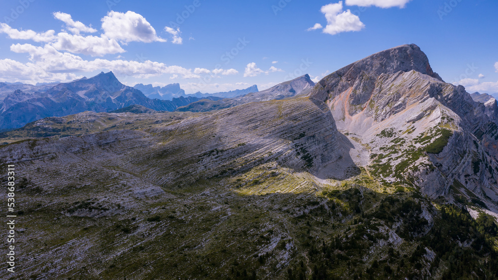 High rocks. Alps in Italy. South Tyrol. Dolomites. Green landscape with stones and green vegetation. Mountain landscape. Shooting from drone. Photo from a copter . Tourism.Blue clouds