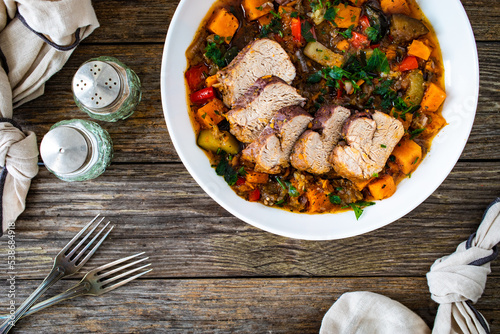 Roast pork loin with sweet potatoes and mix of cooked vegetables served on wooden table

 photo