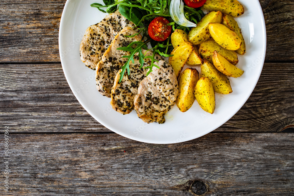 Fried pork loin with baked potatoes and fresh green vegetables on wooden table
Fried pork loin with baked potatoes and fresh green vegetables on wooden table