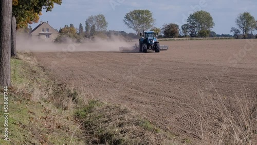 Traktor fährt über ein trockenes und abgeerntetes Feld und wirbelt Staubwolken auf