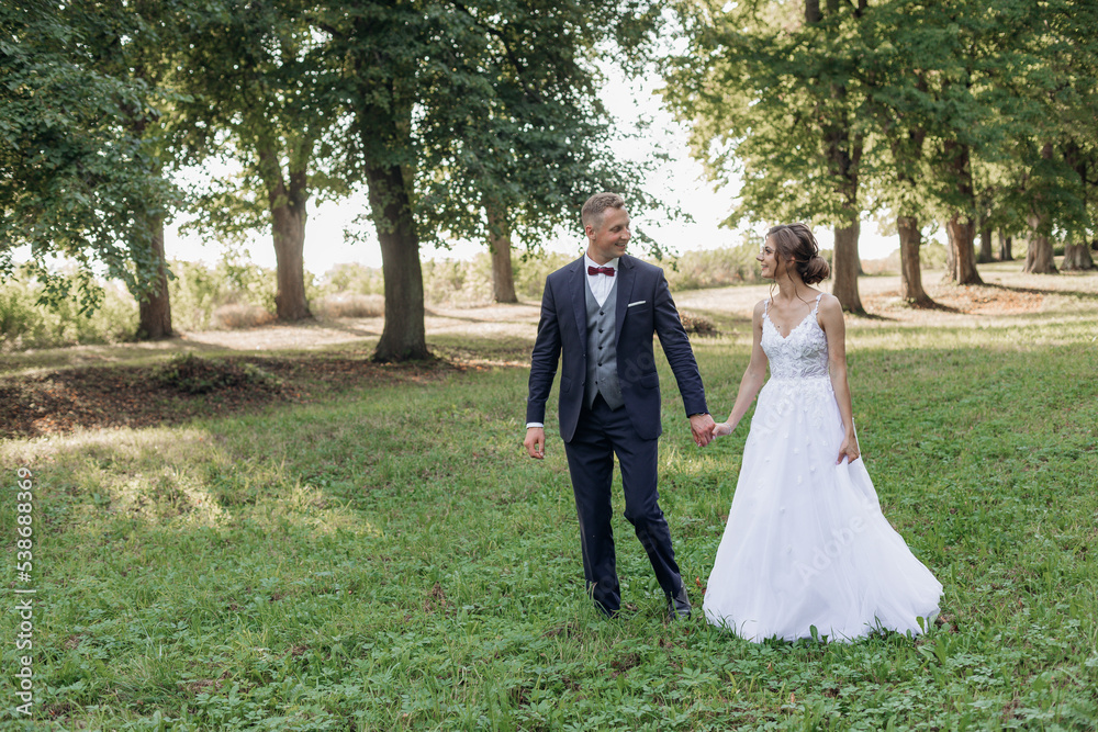 Portrait of happy wedding couple walking on green grass in park in summer. Young attractive woman looking at young man.