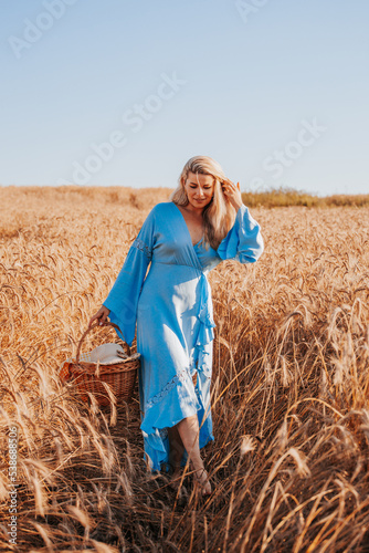 Spectacular charming blonde in a sky blue long light dress among dry grass in a field in the harvest season - rural landscape © andrey gonchar