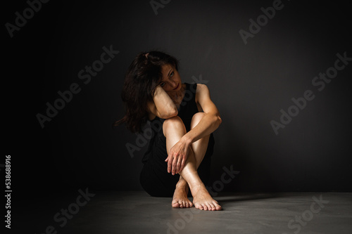 young pretty girl sitting on the floor, pensive, thinking, depression, dark background, low key