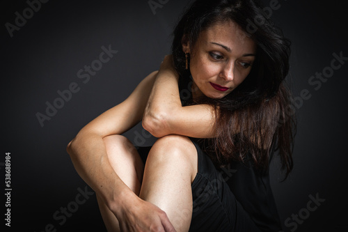 emotional portrait of a young beautiful girl sitting on the floor, pensive, thinking, depression, dark background, low key © Jurii