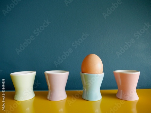 Row of vintage pastel egg cups on yellow sideboard against blue background. photo