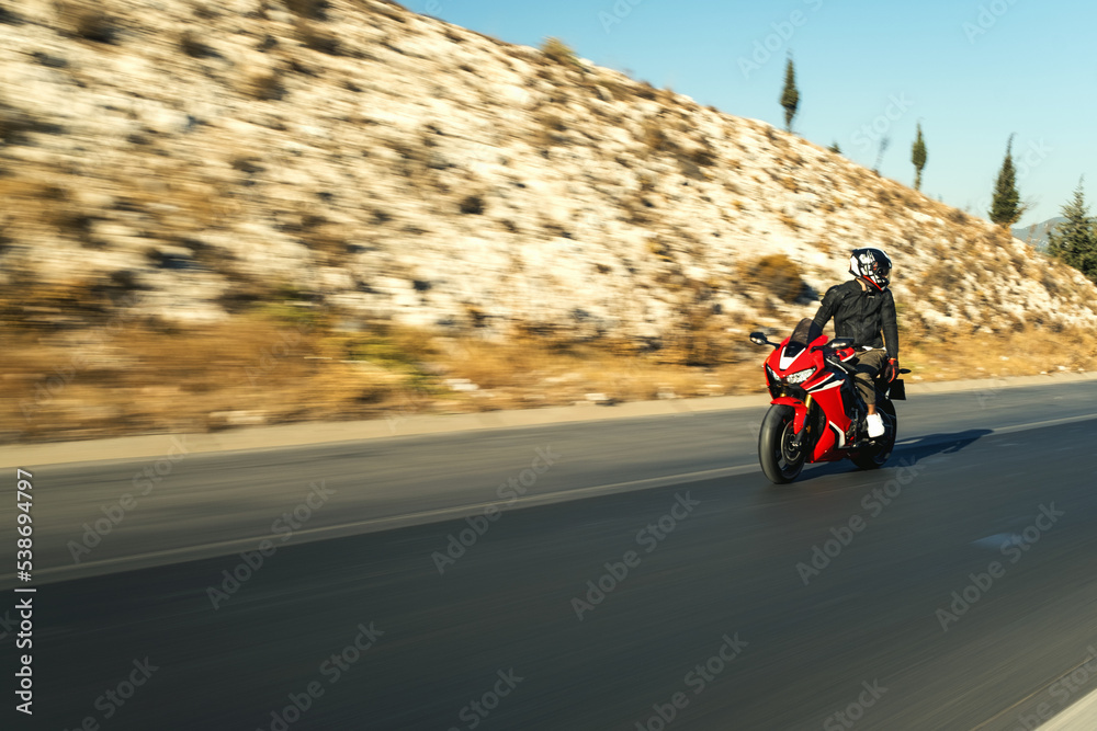 Front view of a motorcycle rider riding red race motorcycle on the highway with motion blur.