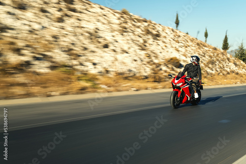 Front view of a motorcycle rider riding red race motorcycle on the highway with motion blur.