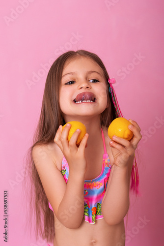 Caucasian beautiful little girl with fresh yellow lemons on a pink background.