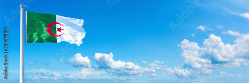 Algeria flag waving on a blue sky in beautiful clouds - Horizontal banner