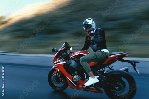 Fototapeta Naklejka Na Ścianę i Meble -  Side view of a motorcycle rider riding red race motorcycle on the highway with motion blur.