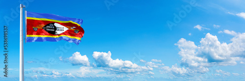 Eswatini flag waving on a blue sky in beautiful clouds - Horizontal banner