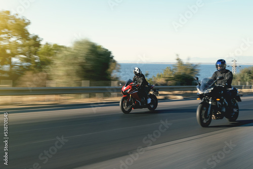 Two supersport race motorcycle riders going fast side by side on the highway with motion blur.