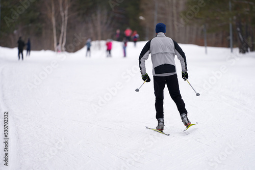 Winter. Weekend. A man is happy to slide on a ski track in the forest. A group of people in the distance. Selective focus.