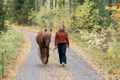 Young woman walking on gravel road with Icelandic horse in autumn scenery. © AnttiJussi