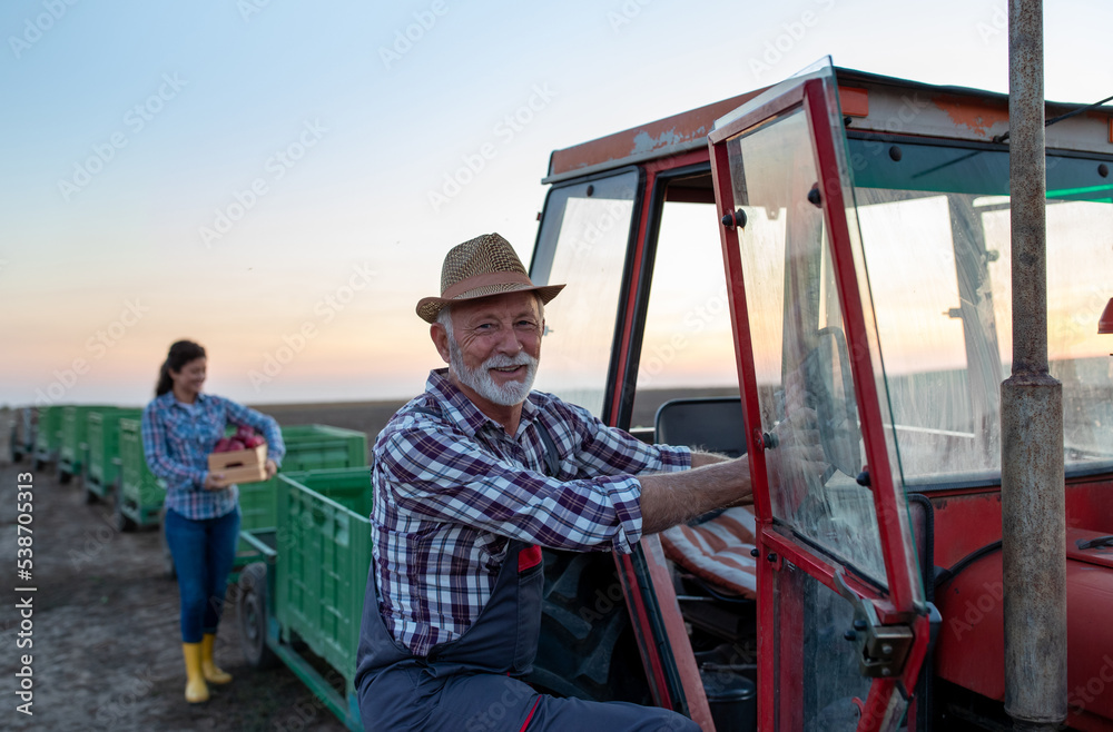 Senior farmer and young woman beside tractor and crates after apple harvest Senior farmer and young woman beside tractor and crates after apple harvest