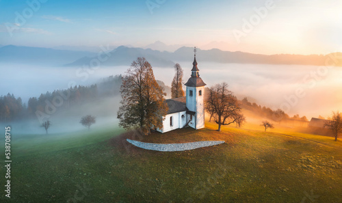 Aerial drone view of small beautiful church on a mountain in Slovenia at dawn. Beautiful autumn morning landscape