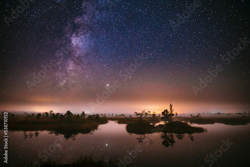 Real Colorful Night Stars Above Swamp. Milky Way Galaxy In Night Starry Sky Above Rural Landscape In Summer Season. Amazing Glowing Stars Effects Above Landscape. Natural Starry Sky Above Landscape.