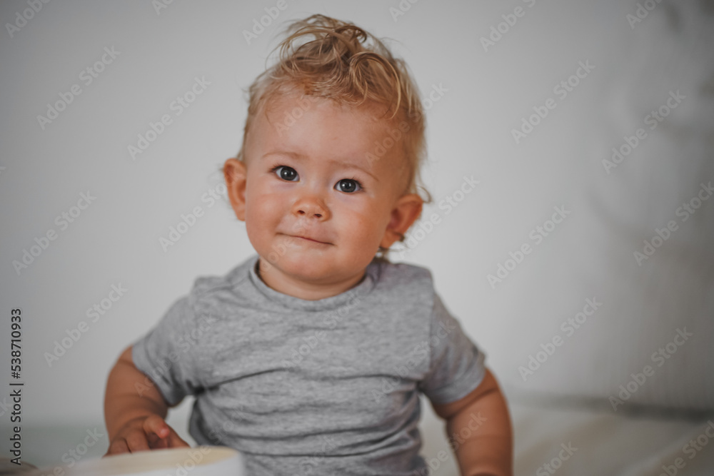 cute happy one year old blond baby boy in casual outfit at home on a cozy sofa smiling or looking into the Camera while open can or box cute happy one year old blond baby boy in casual outfit at home on a cozy sofa smiling or looking into the Camera while open can or box