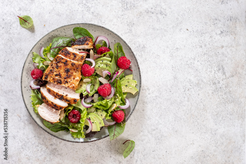 Grilled chicken breast, fillet and fresh vegetable salad of lettuce, arugula, spinach, avocado, onion and pecan nut with raspberry. Summer salad, healthy eating. Fresh healthy food.